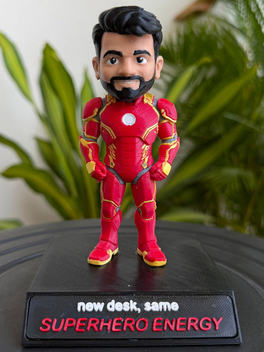 Bobblehead figure of a superhero in a red suit with a plant in the background